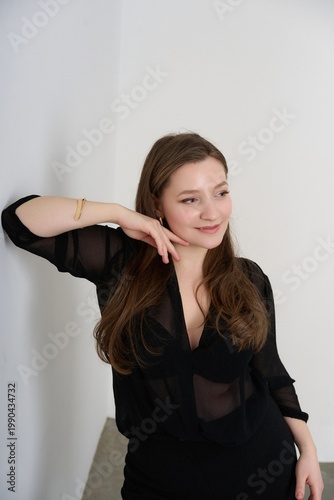 Young woman poses confidently against a wall in a simple black outfit during a casual indoor setting