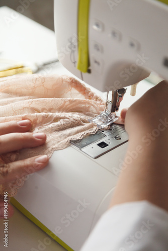 A close-up photo of a seamstress sewing beige lace on a sewing machine. Photo grain added.