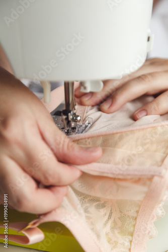 A close-up photo of a seamstress sewing beige lace on a sewing machine. Photo grain added.