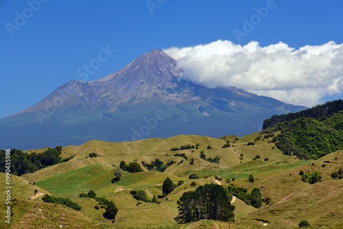 spectacular view of mount taranaki and fanthams peak in egmont national park across rolling farmlands on a  sunny day near te wera on the forgotten world highway on new zealand's north island 