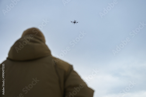 Rear view of soldier observing military drone in flight. Modern warfare scene showing surveillance, control, and дистанція between operator and aerial system.