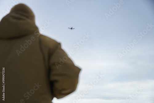 Rear view of soldier observing military drone in flight. Modern warfare scene showing surveillance, control, and дистанція between operator and aerial system.