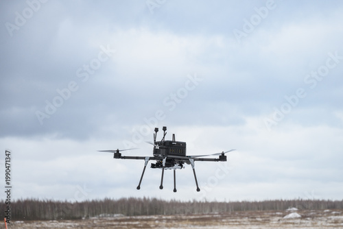 Military bomber drone equipped with payload release system flying over field. Modern aerial warfare technology used for strike missions and tactical operations.