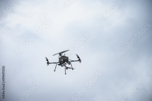 Military bomber drone equipped with payload release system flying over field. Modern aerial warfare technology used for strike missions and tactical operations.