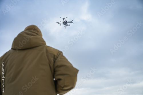 Rear view of soldier observing military drone in flight. Modern warfare scene showing surveillance, control, and дистанція between operator and aerial system.