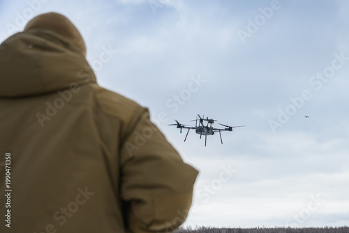 Rear view of soldier observing military drone in flight. Modern warfare scene showing surveillance, control, and дистанція between operator and aerial system.