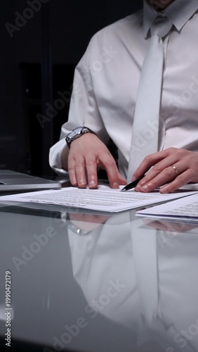 Fotografía Man in white shirt reviewing legal documents, checking details of a contract with a magnifying glass on a dimly lit desk