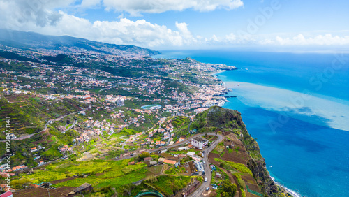 Funchal, Madeira's capital, sprawls across volcanic hillsides to the Atlantic. Lush landscapes meet the vibrant blue ocean under a partly cloudy sky. Cabo Girao