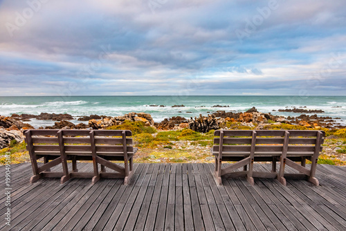 Wooden bench on decking provides idyllic coastal view, tranquil ocean horizon.