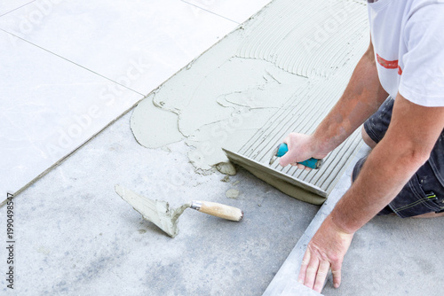 Worker spreading and combing tile adhesive for outdoor patio installation