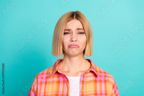 Fotografie Sad young woman making a pouty face in a colorful plaid shirt against a turquois