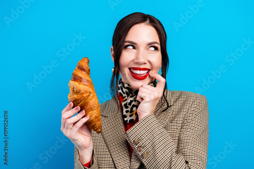Photos Stylish woman holding a croissant and smiling playfully against a bright blue ba