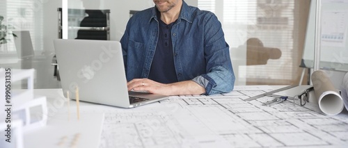 Fotografi Male architect wearing denim shirt working on laptop in modern office, analyzing
