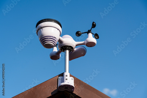 Weather station sensor installed on a rooftop against a clear blue sky, capturing data such as temperature, humidity, and wind speed for accurate forecasts and climate monitoring.