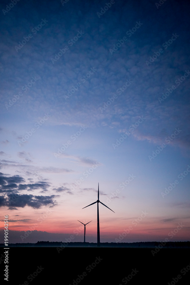 Obraz premium Two wind turbines against a blue and orange sky at sunrise, peaceful atmosphere, view across a misty field to two wind turbines during dawn, near 49424 Goldenstedt, Vechta district, Germany