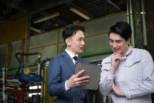 Plakat w ramie 製造業の工場でタブレットを持つ作業員と信金などの打ち合わせをする営業ビジネスマンの2人 設備投資で業務効率などの借り入れのイメージ 左にコピースペースあり