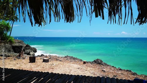 Tropical Ocean View Framed by Traditional Thatched Roof Hut with Turquoise Sea and Rocky Coastline - 4K footage