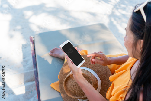 Asian woman using mobile phone while relaxing at the beach. Summer and vacation, Technology and lifestyle concept. Copy space