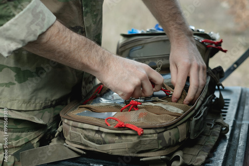 Military paramedic hands near open backpack with first aid kit, close up