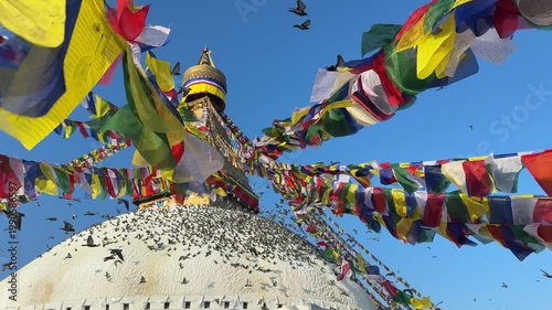 Slow motion pigeons flying around Boudhanath stupa in Kathmandu with colorful prayer flags waving in the wind. Spiritual atmosphere, Buddhism, travel, peaceful scene, cultural landmark