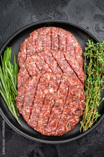 Raw mixed meat patties for Hamburger made from beef and lamb with herbs in plate. Dark rustic stone background with copy space for menu use.