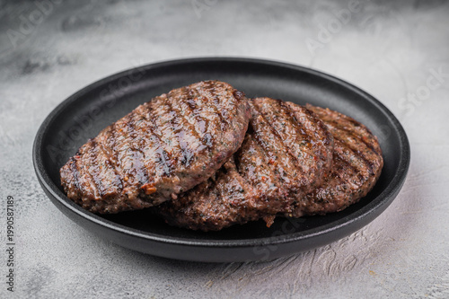 Fried mixed meat patties for burgers made from beef and lamb in skillet with herbs. Light stone background with copy space for menu design.