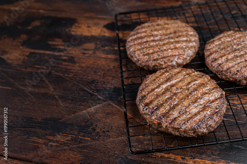 Grilled beef and lamb patties with seared crust and juicy texture on metal rack. Cooked mixed meat cutlets on dark wooden background.