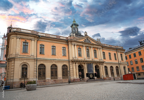 The historic Nobel Prize Museum building stands in the center of Stortorget square in Stockholm's old town under a dramatic sunset sky.