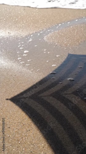 Shadow of striped beach umbrella on sand near water, summer beach scene.