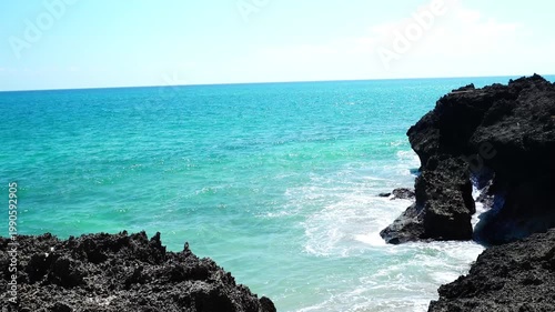 Waves Crashing Against Rugged Rocky Cove with Turquoise Ocean and Clear Sky on Tropical Coast - 4K footage