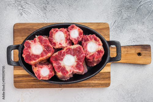 Foto Butcher style raw oxtail in skillet on wooden board, collagen rich beef cut for