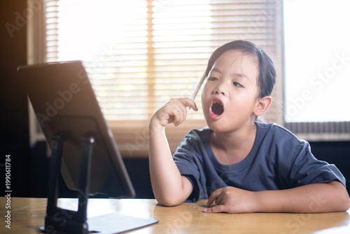 Curious young Asian girl thinking and talking during online class with tablet, little child learning language or practicing speech with digital device at home.