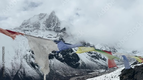 Tibetan prayer flags fluttering against cloudy snowy mountains in Everest region, Nepal. Dramatic Himalayan landscape with mist and moving clouds, atmospheric slow motion shot