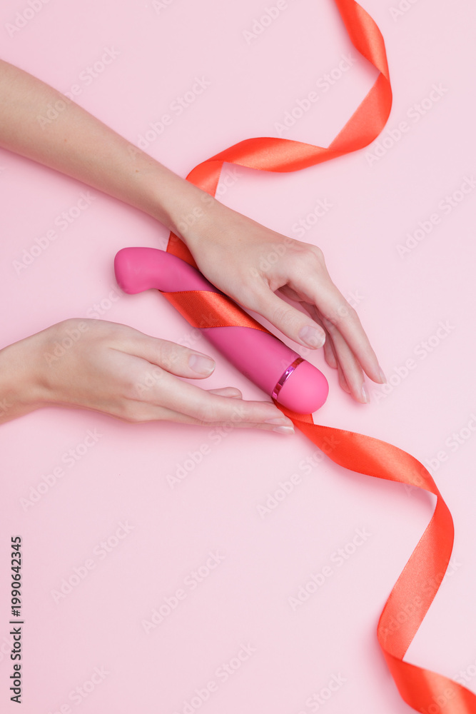 Naklejka premium Pink vibrator on pink background with red ribbon and caucasian female hands