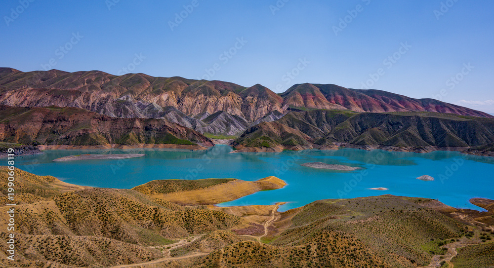 Naklejka premium Turquoise lake surrounded by colorful mountain ridges under bright sky