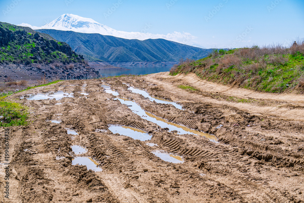 Fototapeta premium Muddy trail with water puddles near forested hills
