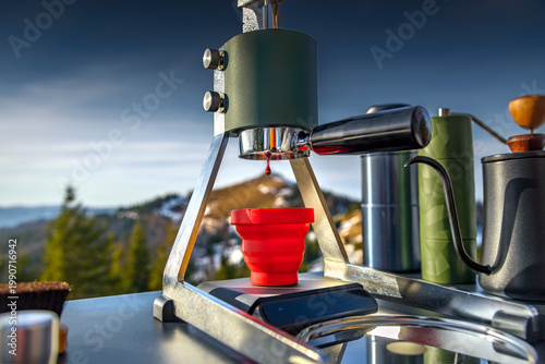 Manual lever espresso machine outdoors, extraction dripping shot, portable coffee setup in mountains