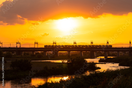 夕日の中で河川に敷かれた鉄橋と通行する電車