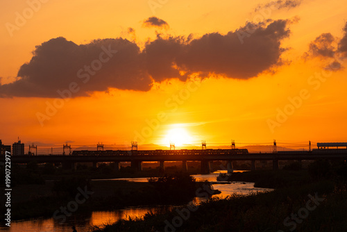 夕日の中で河川に敷かれた鉄橋と通行する電車