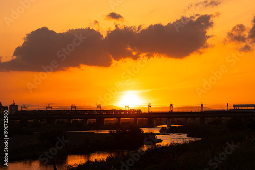 夕日の中で河川に敷かれた鉄橋と通行する電車
