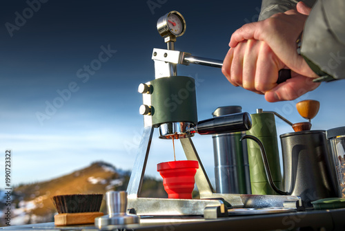 Man brewing espresso with manual lever coffee maker in mountains. Outdoor barista travel lifestyle