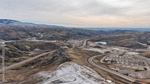 Aerial View of Mountain Highway Corridor Through Snow-Dusted Hills with New Subdivision Development and Overcast Sky