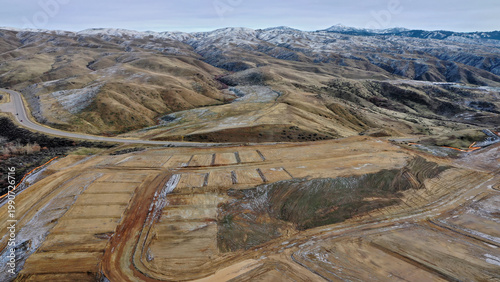 Aerial View of Terraced Hillside Land Grading and Development with Snow-Capped Mountain Range in Background