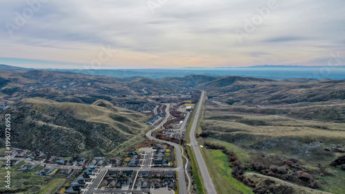 Aerial View of Mountain Highway Through Rolling Hills with Suburban Subdivision Development in Foreground Under Overcast Sky
