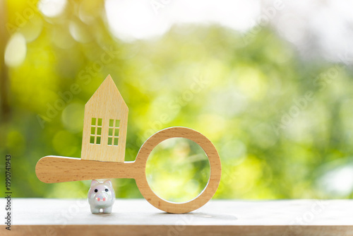 The image from the mirrorless camera shows a Piggy bank hold a magnifier with searching for new home in the public park, Loan for real estate or saving for buy house concept.