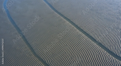 Aerial view of sand with intricate wavy patterns and two dark lines running through it