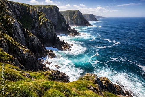 Rocky cliffs with green grass and moss on a sunny day by the ocean with crashing waves and blue water under a blue sky