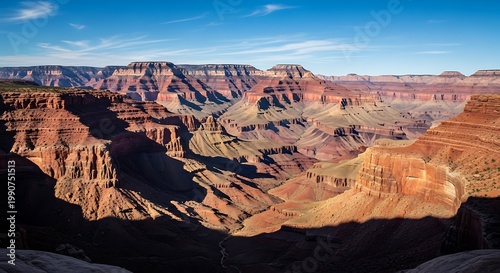 Grand Canyon landscape with deep red and orange rocky formations under a clear blue sky with wispy clouds