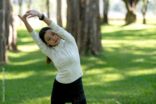 Young Asian Woman Doing Side Stretch Exercise in Sunny Park with Trees