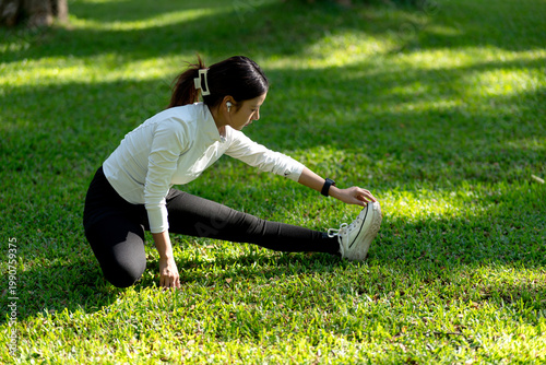 Foto Young Asian Woman Stretching Leg Muscles on Green Grass in Park Before Outdoor W